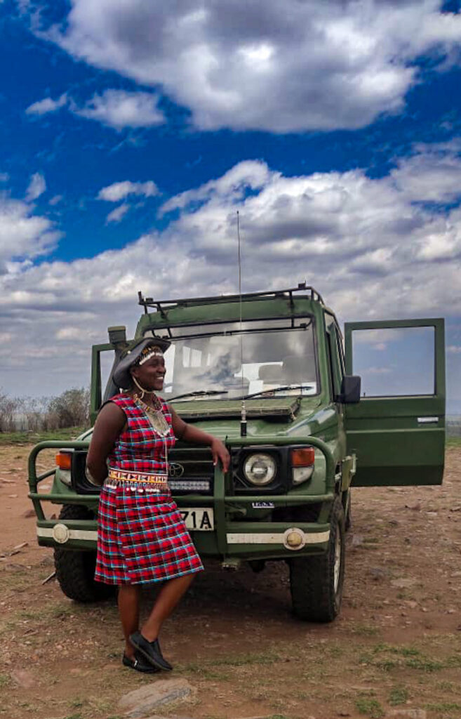 Certified female safari guide Magdaline Muindi in traditional attire by her 4x4 land cruiser