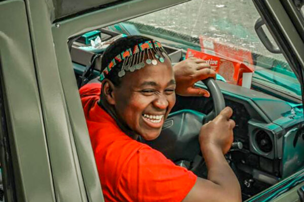 Certified female safari guide Magdaline Muindi in traditional attire by her 4x4 land cruiser.
