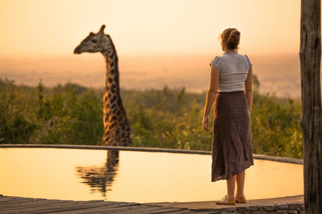 Solo female guest standing by a safari lodge pool observing a giraffe on a solo female safari Kenya trip.