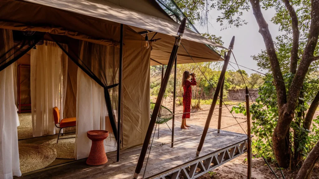 Solo female guest standing on a safari tent veranda using binoculars on a solo female safari Kenya trip