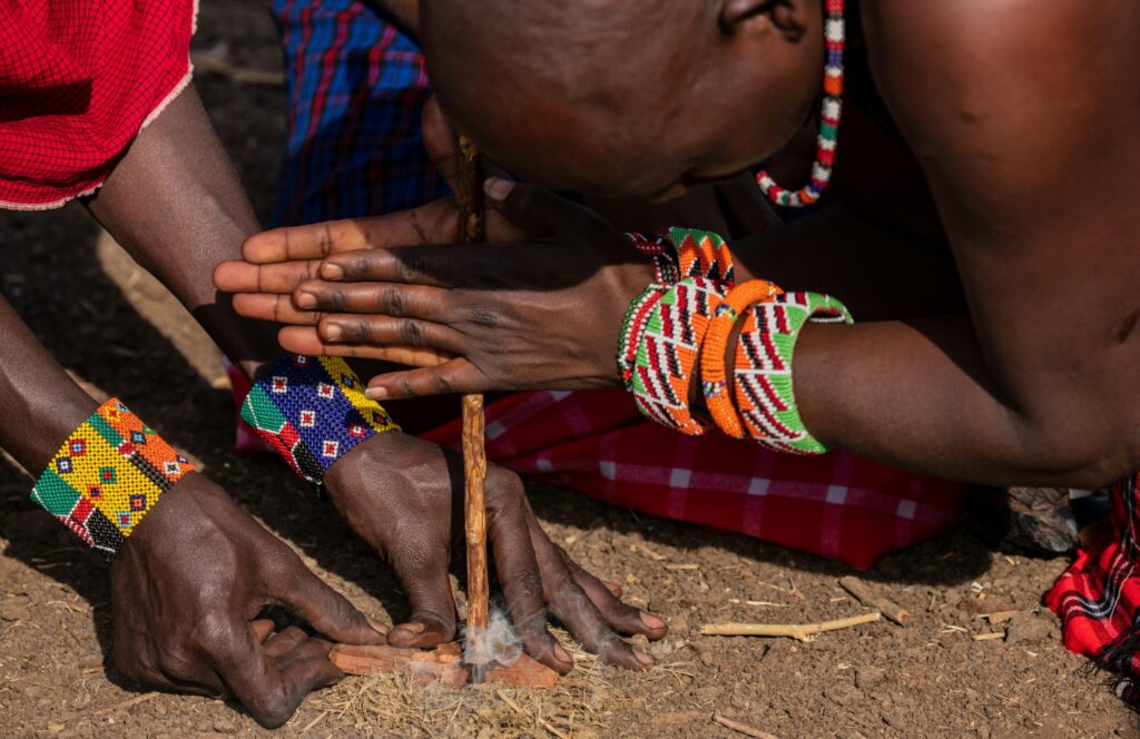 Maasai men demonstrating traditional fire making by friction during a guided Maasai village visit Kenya.